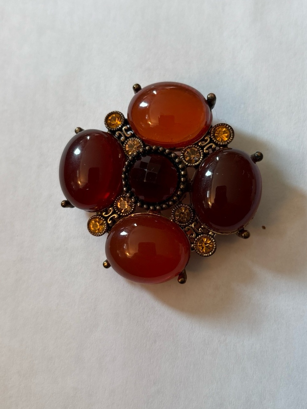 Amber/ orangish/red tone brooch set in gold tone metal.